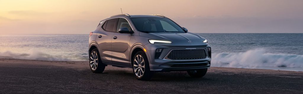 2026 Buick Encore GX parked beach side with a sleek coupe-inspired SUV design, wheels, and distinctive LED lighting near Stadium Buick GMC in Salem, OH.